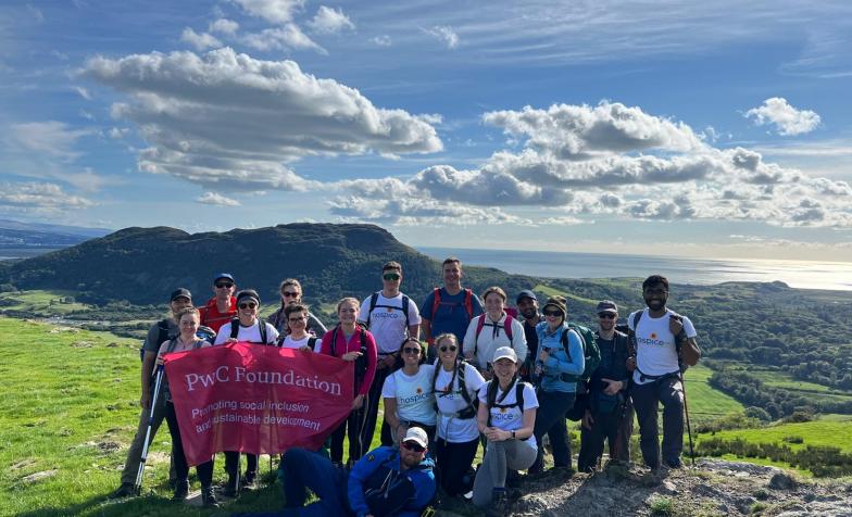 Group on top of a mountain in white Hospice UK t-shirts holding pink PwC banner