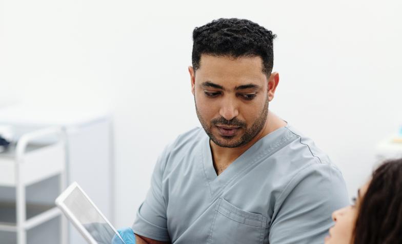 Male nurse wearing scrubs showing a tablet screen to female patient
