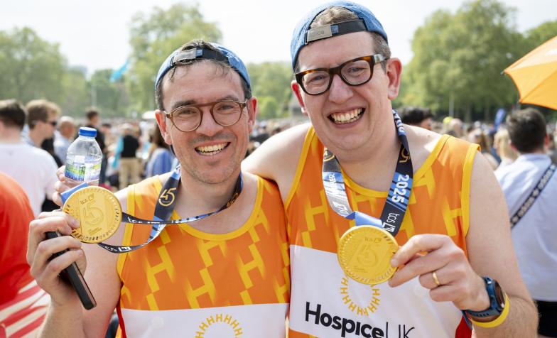 Two smiling runners, wearing Hospice UK vests and holding up their London Marathon medals
