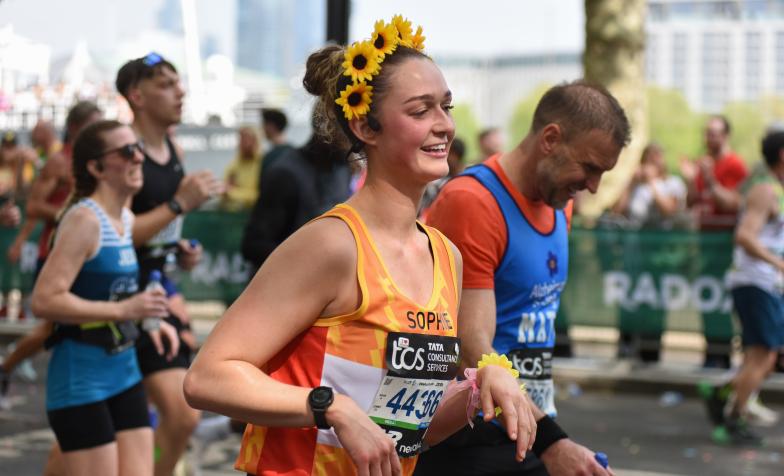 woman running with sunflower headband and orange Hospice UK branded vest