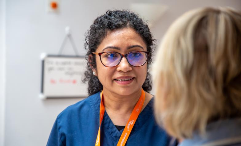 Doctor wearing blue scrubs and wearing a orange lanyard. The back of someone's head is in the foreground on the right.