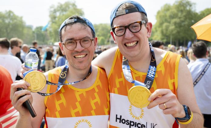 Two smiling runners, wearing Hospice UK vests and holding up their London Marathon medals
