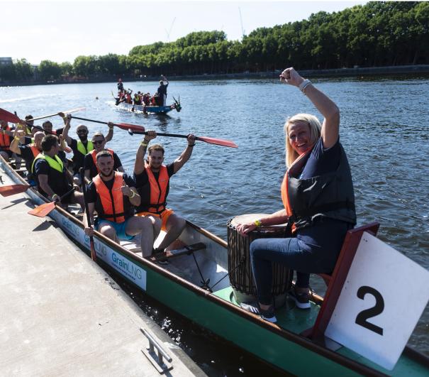 Dragon boat race team sat in boat smiling and waving
