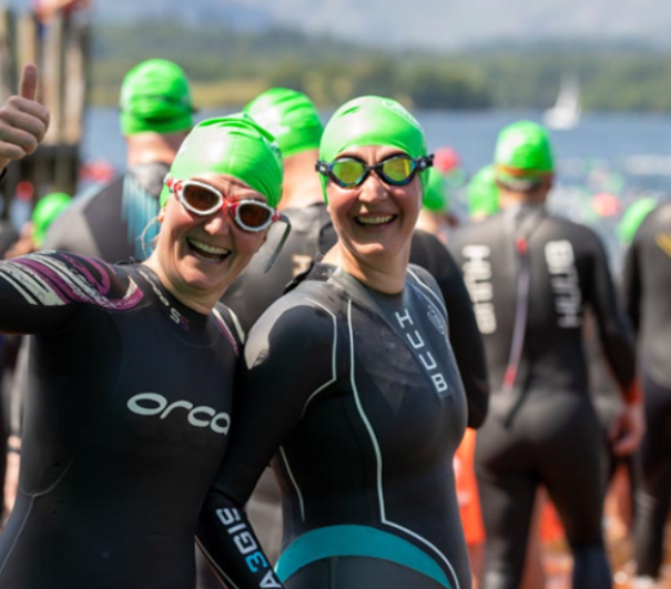 2 female swimmers with wetsuits and green swimming caps smiling