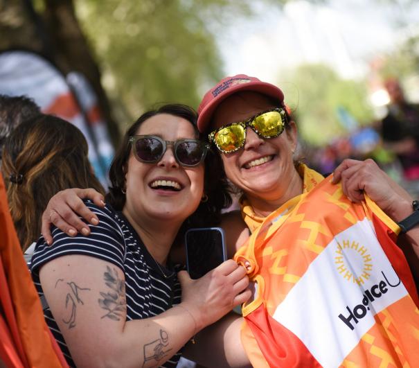 Two people hugging, with one holding up a Hospice UK running vest 