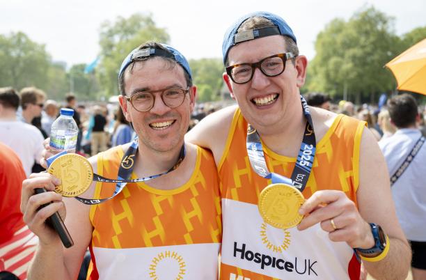 Two smiling runners, wearing Hospice UK vests and holding up their London Marathon medals