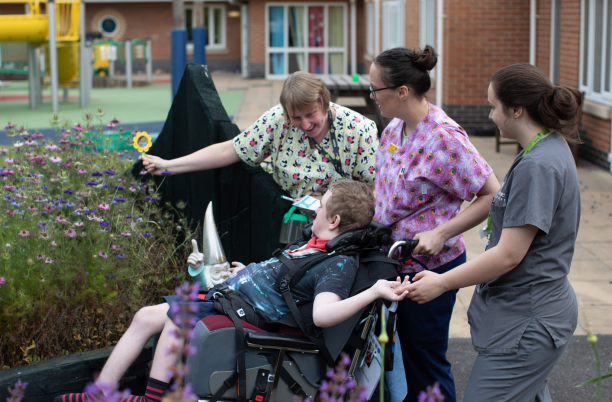 A group of people caring for a young person in a wheelchair in a hospice garden
