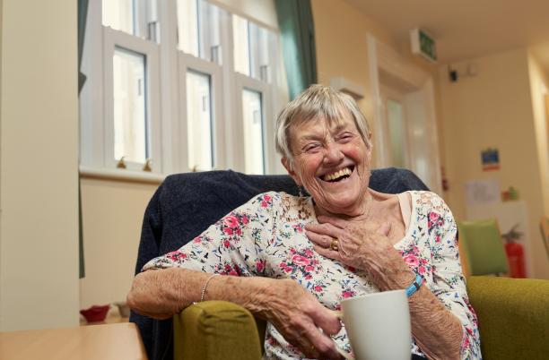 Woman sat in a chair laughing with a cup of tea