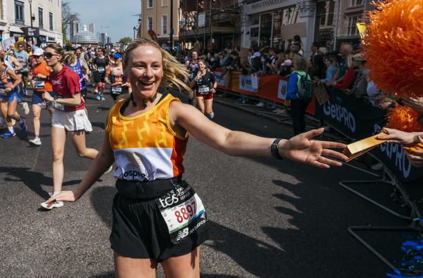 Woman running wearing a Hospice UK vest and high fiving a supporter on the sidelines