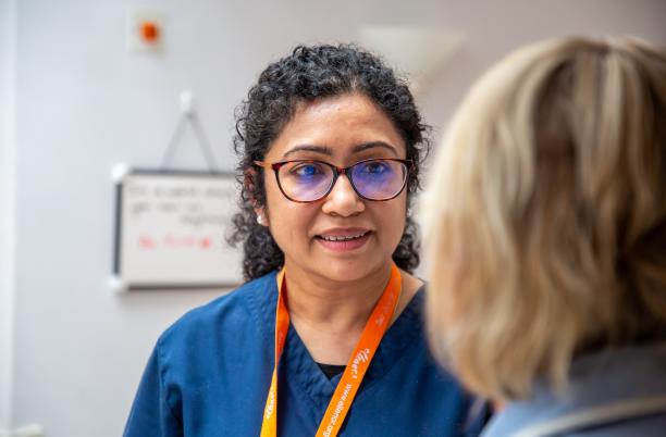 Doctor wearing blue scrubs and wearing a orange lanyard. The back of someone's head is in the foreground on the right.