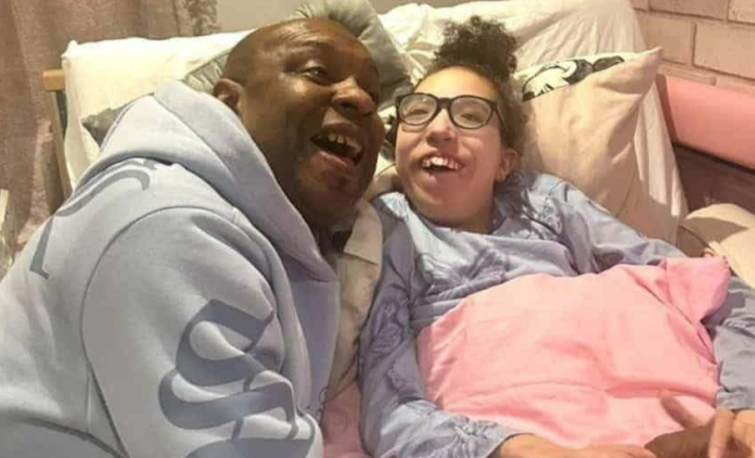 A dad is smiling next to his daughter, who is lying in bed. They both look very happy.