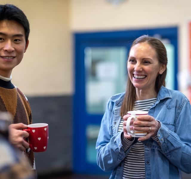 Waist-up shot of a group of adults getting together in a community hall and having a cup of tea together.
