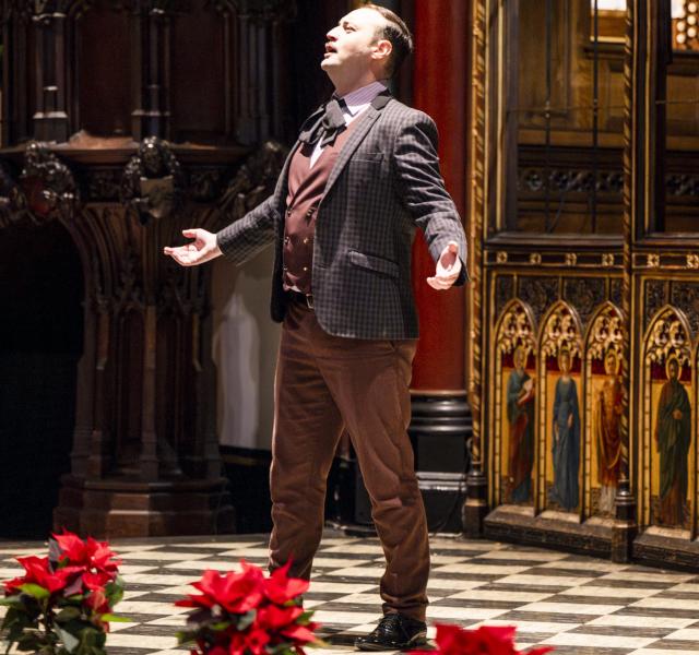 A male performer singing at the front of a church, dressed in a suit