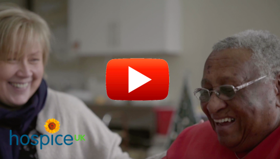 Two women laughing in a hospice setting with a play button in the middle of the image