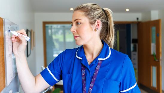 A nurse at Royal Trinity Hospice completing a whiteboard of information