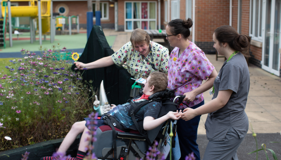 A group of people caring for a young person in a wheelchair in a hospice garden